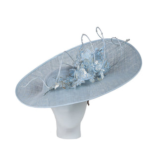 Britsh hat designer, large light blue hat with floral embellishments on a white background