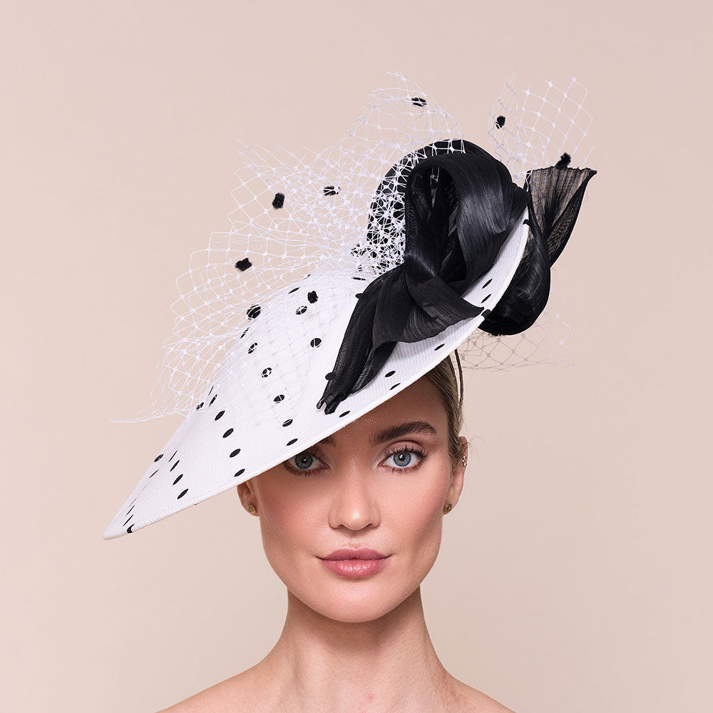 Hat for the Ascot Royal enclosure, white hat with black polka dots and decorative elements on a beige background