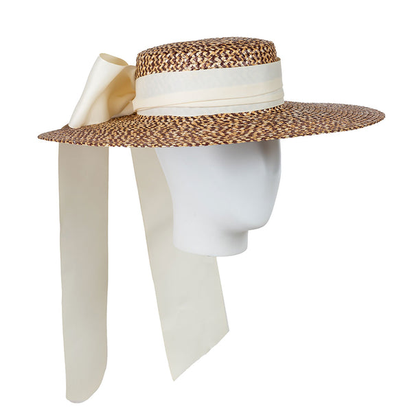 Wide-brimmed straw hat with a white ribbon on a mannequin head against a white background