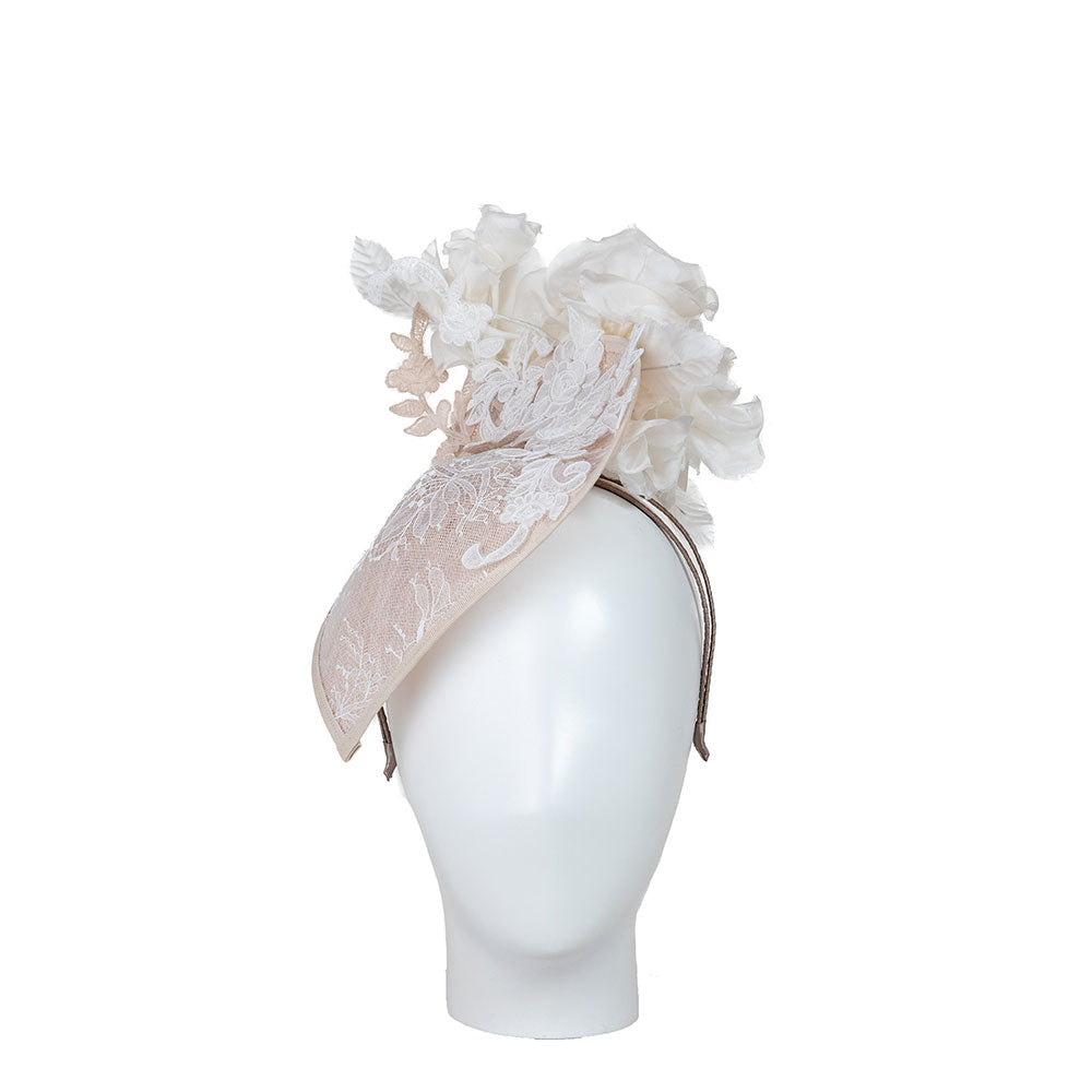 Woman wearing a high end wedding hat - a white lace headpiece. Photo against a beige background