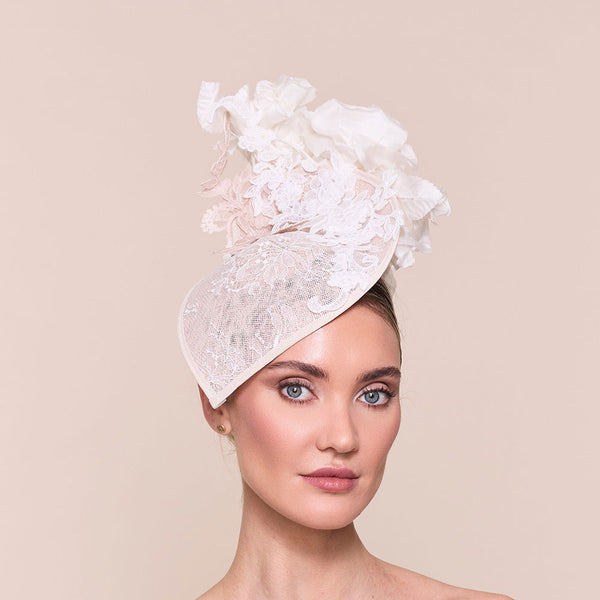 Woman wearing a high end wedding hat - a white lace headpiece. Photo against a beige background