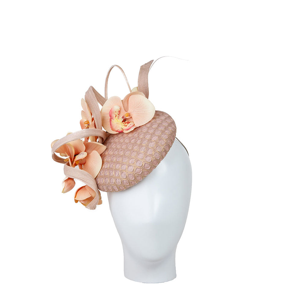 Woman wearing a mother of the bride hat, in pink with decorative flowers. Photo on a beige background