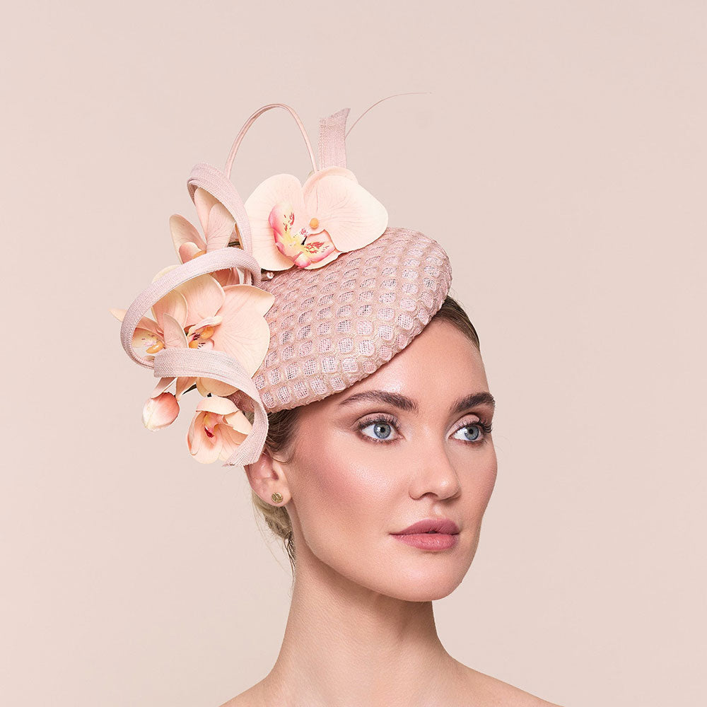 Woman wearing a mother of the bride hat, in pink with decorative flowers. Photo on a beige background